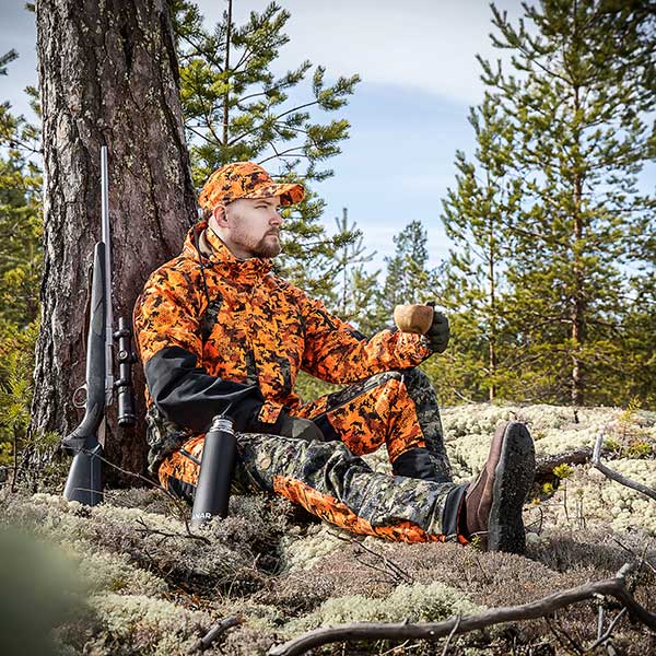 Mies istuu luonnossa Anar Hirvas -metsätyspuvussa.